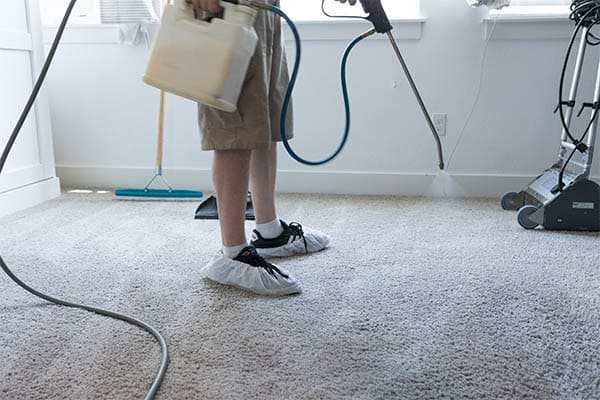 Uniformed MSS Cleaning employee pre-spraying carpet with a power sprayer prior to hot water extraction