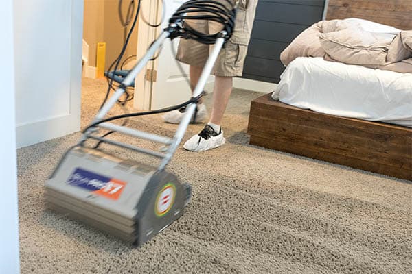 Uniformed MSS Cleaning employee using counter rotating brush machine to deep clean carpet