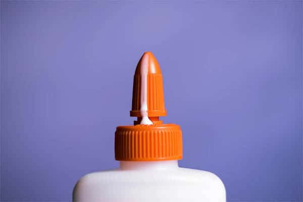 bottle of glue with orange cap covered in white glue