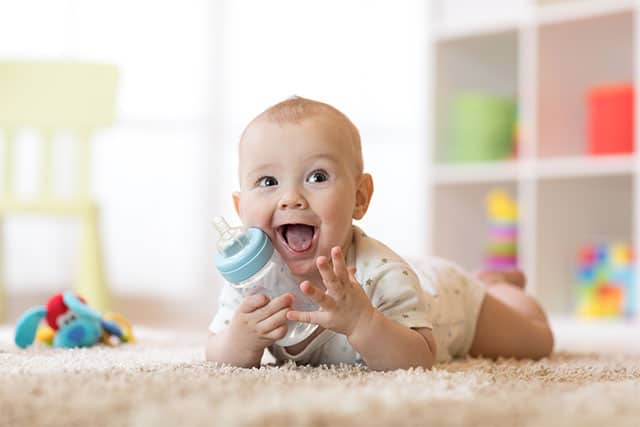 baby with bottle of milk lying on carpet